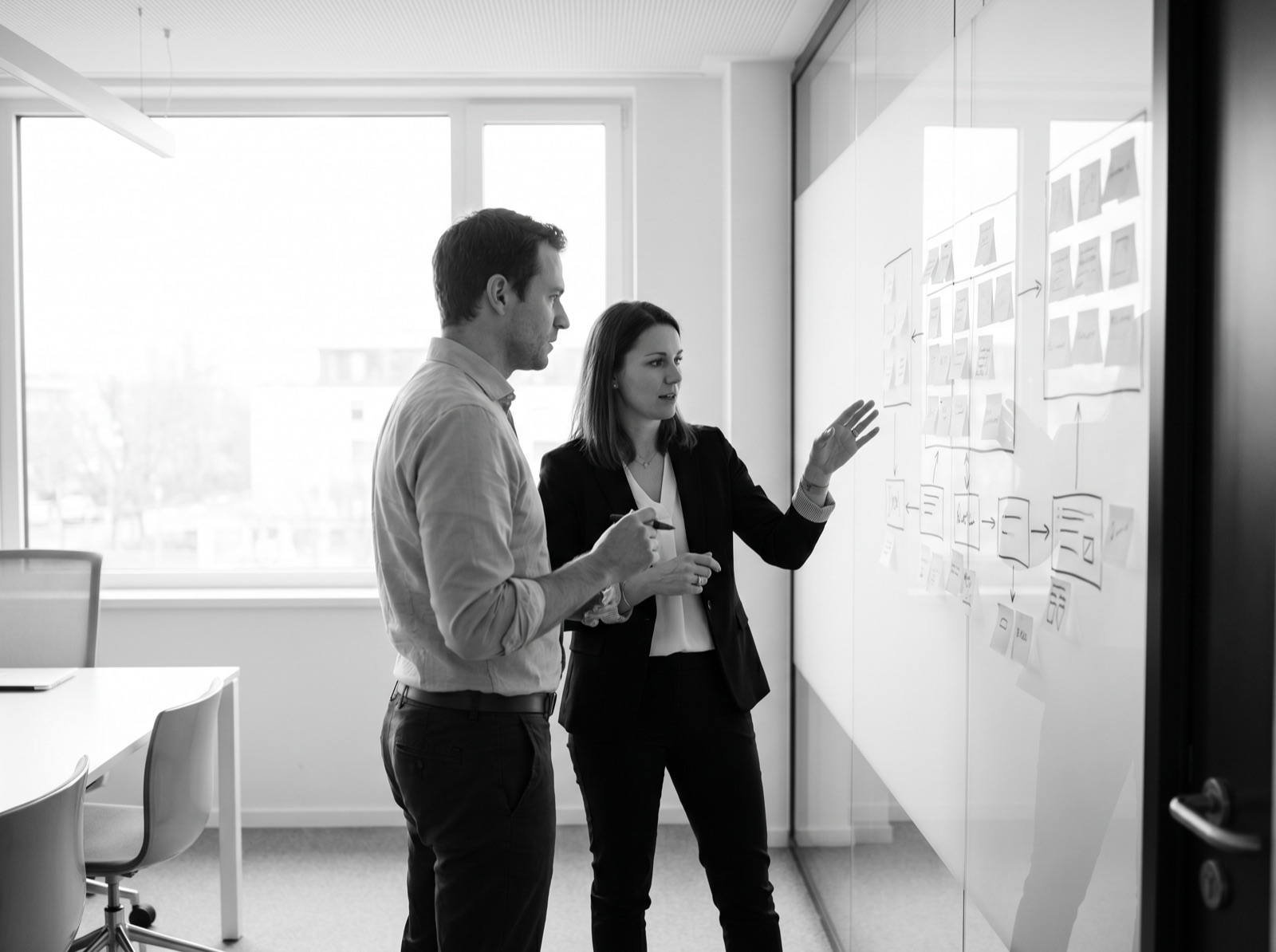 Two people planning a website structure on a glass wall of sticky notes